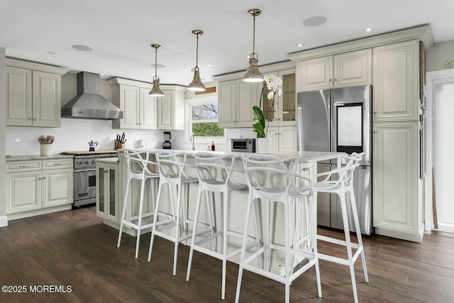 kitchen with a breakfast bar area, dark wood-style floors, stainless steel appliances, wall chimney range hood, and backsplash