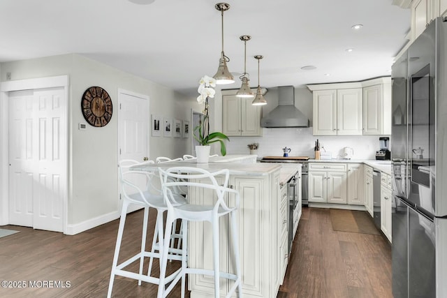 kitchen featuring a center island, dark wood-type flooring, a breakfast bar, appliances with stainless steel finishes, and wall chimney exhaust hood