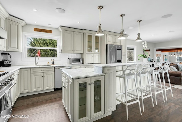 kitchen with a sink, a kitchen breakfast bar, dark wood finished floors, appliances with stainless steel finishes, and glass insert cabinets