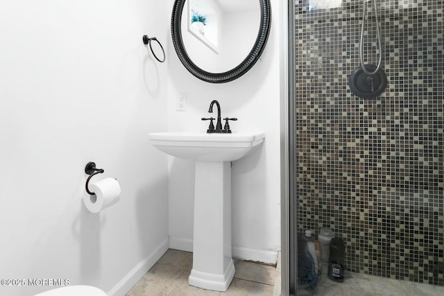 bathroom with tile patterned flooring, tiled shower, baseboards, and a sink