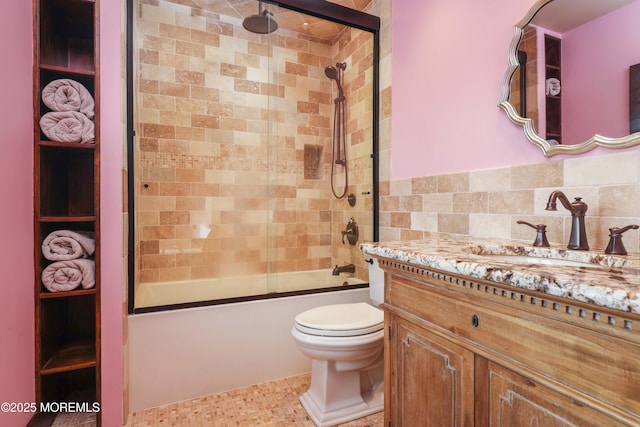bathroom with vanity, toilet, tile walls, and bath / shower combo with glass door