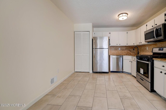 kitchen with appliances with stainless steel finishes, white cabinetry, visible vents, and tasteful backsplash