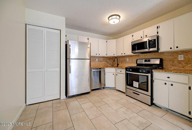 kitchen featuring stainless steel appliances, decorative backsplash, white cabinets, a sink, and light stone countertops