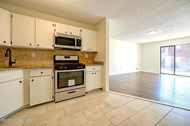 kitchen featuring light stone counters, a sink, white cabinets, appliances with stainless steel finishes, and tasteful backsplash