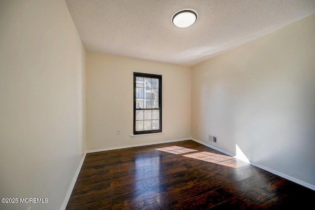 spare room featuring wood-type flooring, visible vents, baseboards, and a textured ceiling