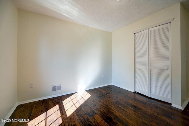 unfurnished bedroom with baseboards, a textured ceiling, visible vents, and dark wood-style flooring