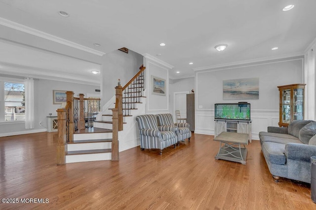 living area with wood finished floors, stairway, a decorative wall, wainscoting, and crown molding