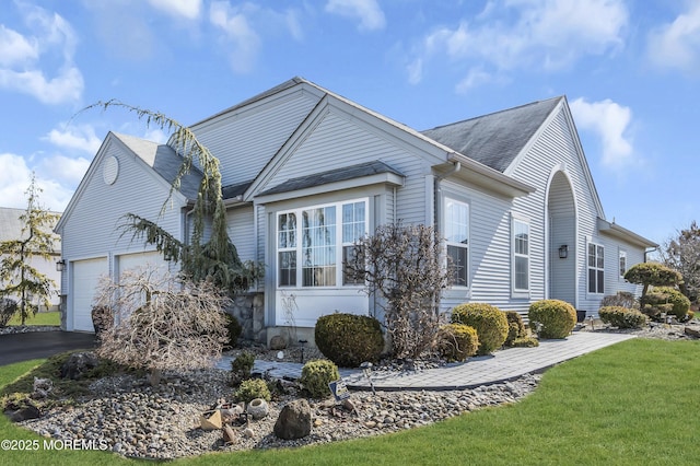 view of side of property with driveway, a yard, an attached garage, and a shingled roof