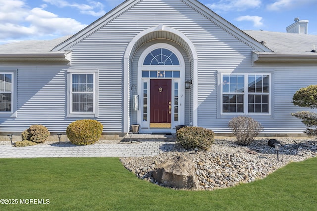 doorway to property with a yard and a shingled roof