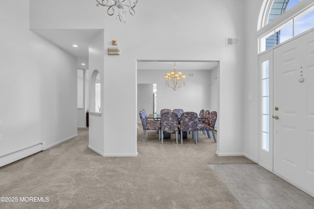 carpeted entrance foyer with visible vents, arched walkways, a towering ceiling, baseboard heating, and a chandelier