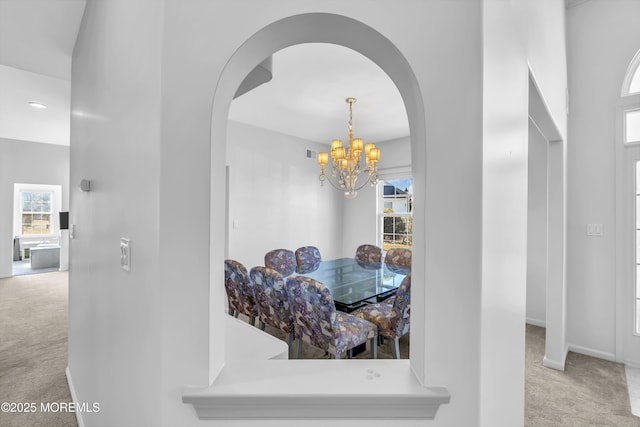 carpeted dining room with an inviting chandelier, baseboards, and arched walkways