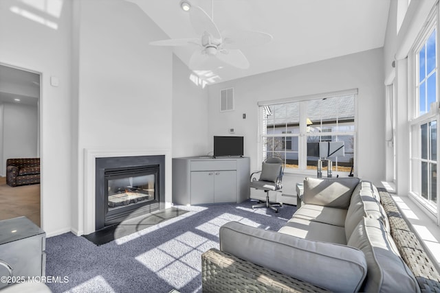 living room with carpet floors, a high ceiling, visible vents, a ceiling fan, and a glass covered fireplace