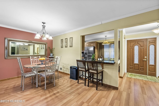 dining space with a notable chandelier, light wood-style flooring, baseboards, and crown molding