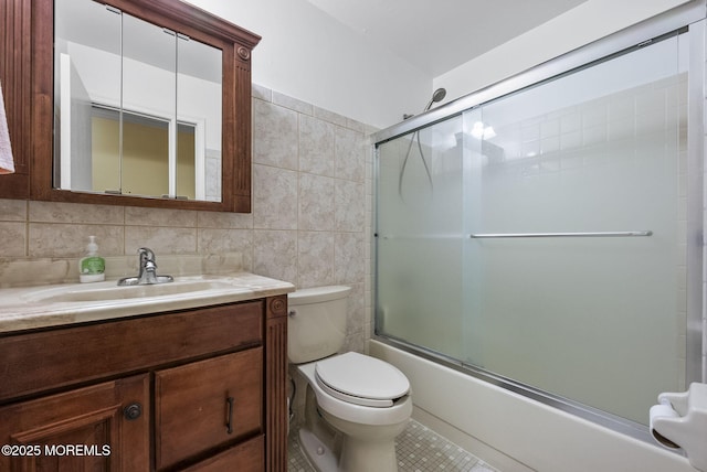 bathroom featuring tile patterned flooring, toilet, bath / shower combo with glass door, vanity, and tile walls