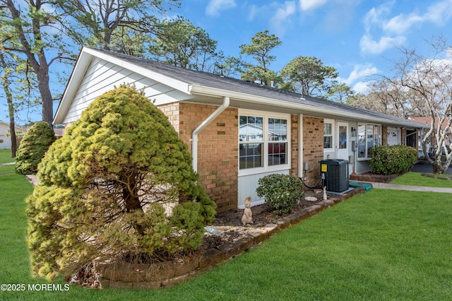 view of side of home with brick siding, a yard, and central air condition unit