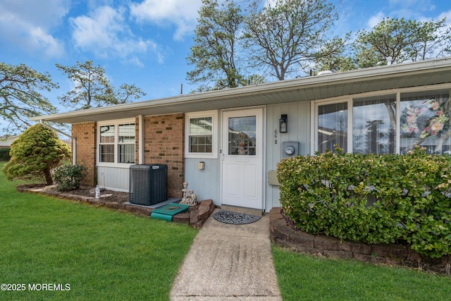 view of exterior entry with central AC, brick siding, and a lawn