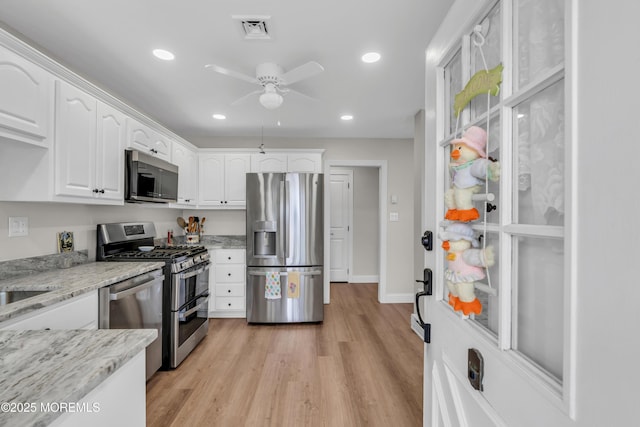 kitchen with visible vents, light wood-style flooring, light stone countertops, stainless steel appliances, and white cabinetry