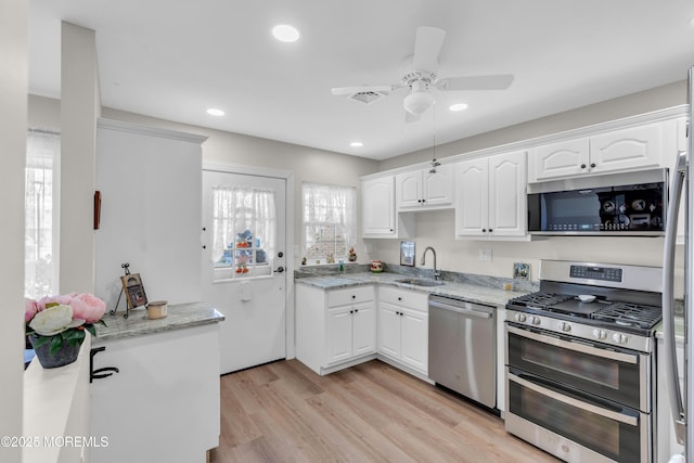 kitchen with light wood-style flooring, light stone counters, stainless steel appliances, white cabinetry, and a sink