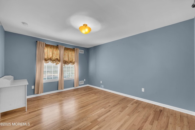 spare room with wood finished floors, visible vents, and baseboards