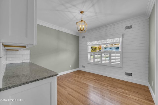 unfurnished dining area with ornamental molding, light wood-type flooring, visible vents, and baseboards