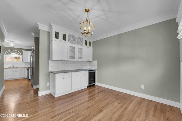 kitchen with beverage cooler, white cabinetry, crown molding, and a sink