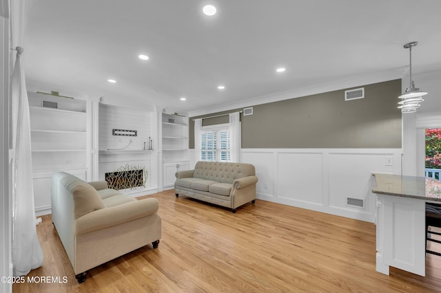 living room with built in shelves, light wood-type flooring, visible vents, and crown molding