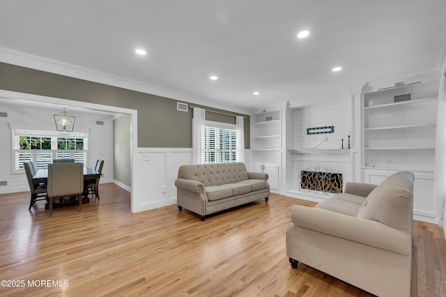 living room featuring built in features, visible vents, light wood-style floors, and ornamental molding