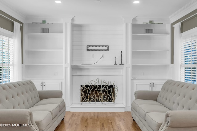 living room featuring a large fireplace, light wood-style flooring, visible vents, and built in features