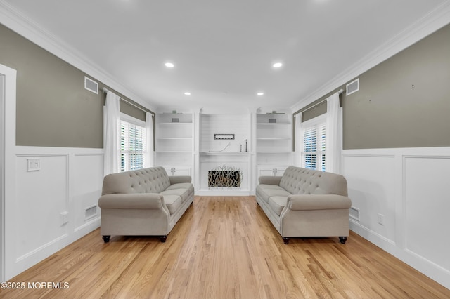 living area with light wood finished floors, visible vents, a decorative wall, and crown molding