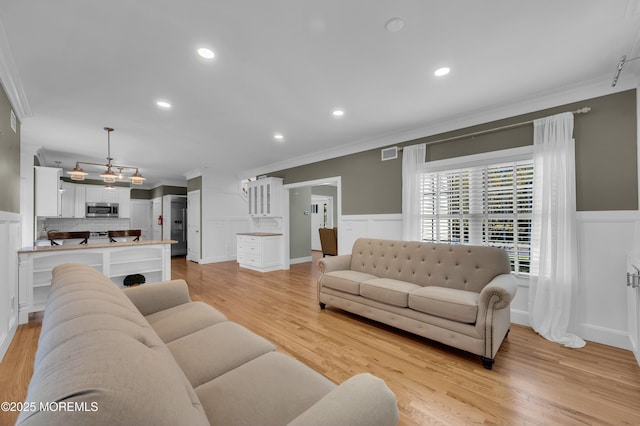 living area with ornamental molding, wainscoting, visible vents, and light wood-style floors