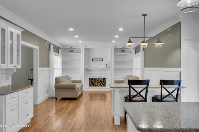 interior space featuring visible vents, wainscoting, light wood-style flooring, ornamental molding, and a fireplace