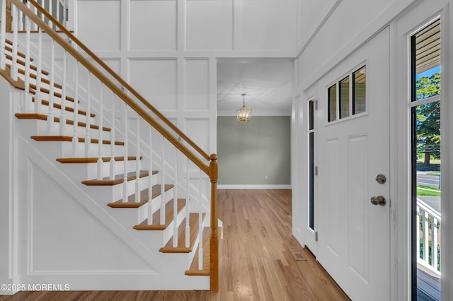 foyer with baseboards, ornamental molding, stairs, light wood-type flooring, and a decorative wall