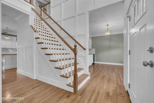 staircase with ornamental molding, a decorative wall, and wood finished floors