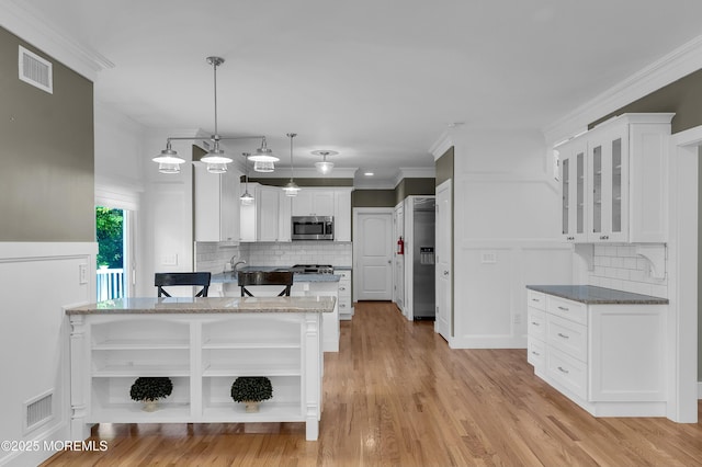 kitchen with visible vents, white cabinets, stainless steel microwave, ornamental molding, and open shelves