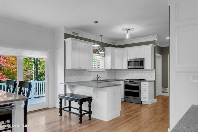 kitchen featuring a breakfast bar area, a peninsula, a sink, white cabinets, and appliances with stainless steel finishes