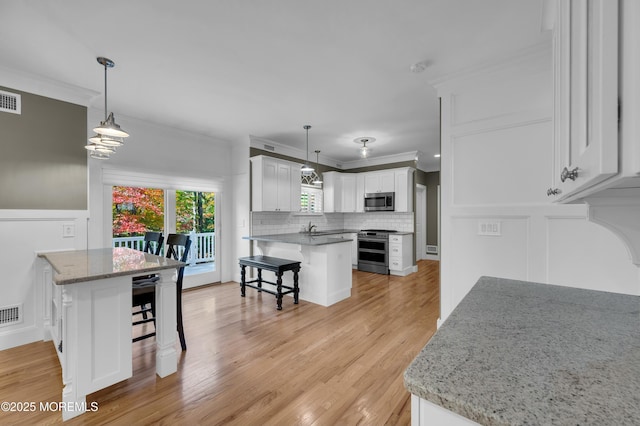 kitchen with crown molding, a breakfast bar area, stainless steel appliances, white cabinetry, and a peninsula