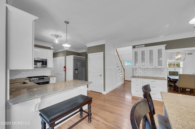 kitchen with glass insert cabinets, ornamental molding, stainless steel appliances, light wood-style floors, and white cabinetry