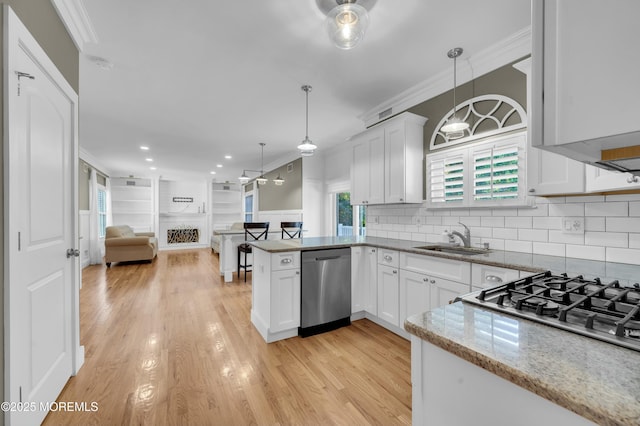 kitchen featuring a sink, white cabinets, open floor plan, stainless steel dishwasher, and ornamental molding