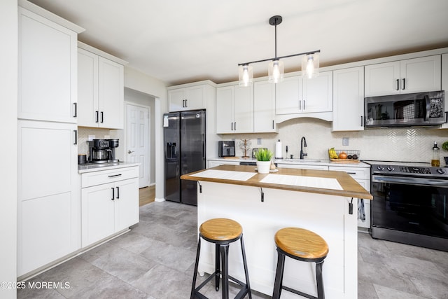 kitchen featuring a sink, hanging light fixtures, stainless steel appliances, wood counters, and a kitchen bar