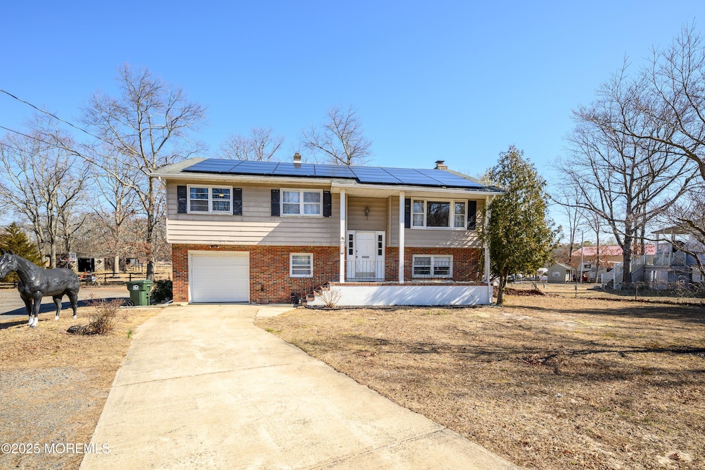 raised ranch featuring roof mounted solar panels, brick siding, covered porch, and concrete driveway