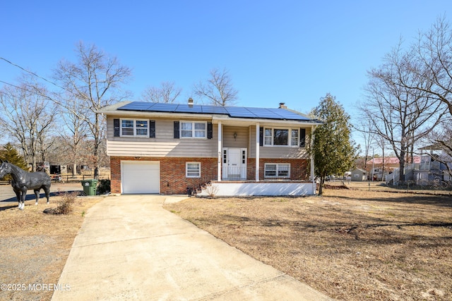 raised ranch featuring roof mounted solar panels, brick siding, covered porch, and concrete driveway