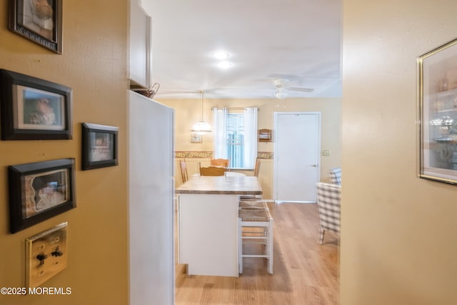 kitchen featuring light wood-style flooring, a ceiling fan, freestanding refrigerator, a breakfast bar area, and light countertops