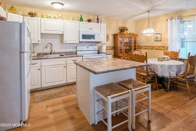 kitchen with white appliances, white cabinetry, light wood-type flooring, and a sink