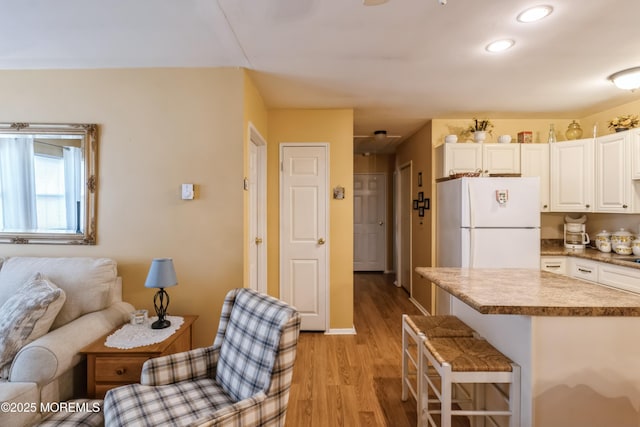 kitchen featuring open floor plan, a breakfast bar area, light wood-style flooring, freestanding refrigerator, and white cabinetry