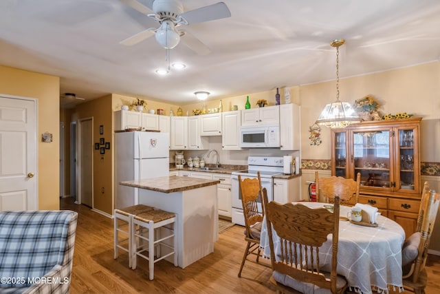 kitchen featuring a kitchen island, ceiling fan, white cabinets, white appliances, and a sink