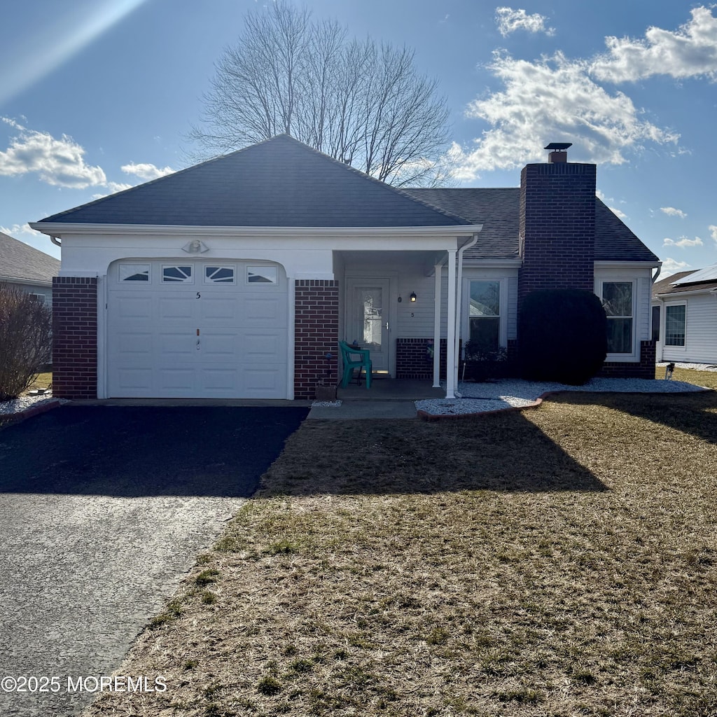 ranch-style home with brick siding, a chimney, a garage, driveway, and a front lawn