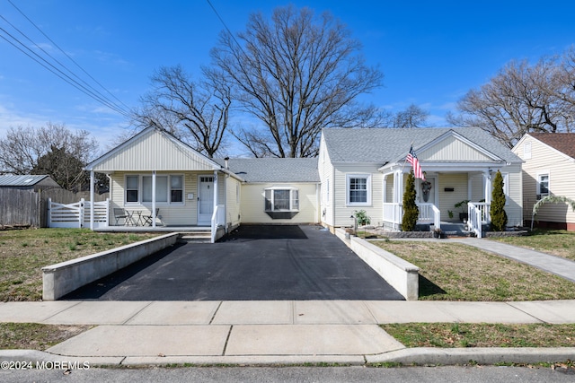 bungalow-style house with a porch, fence, driveway, and a shingled roof