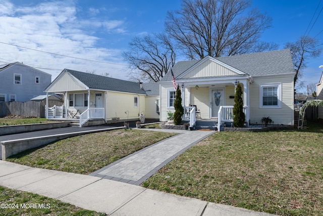 bungalow-style home featuring a porch, roof with shingles, fence, and a front lawn