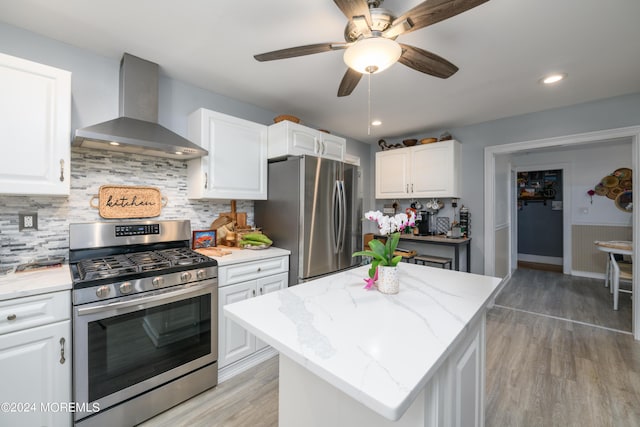 kitchen with light wood finished floors, wall chimney exhaust hood, light stone countertops, stainless steel appliances, and white cabinetry