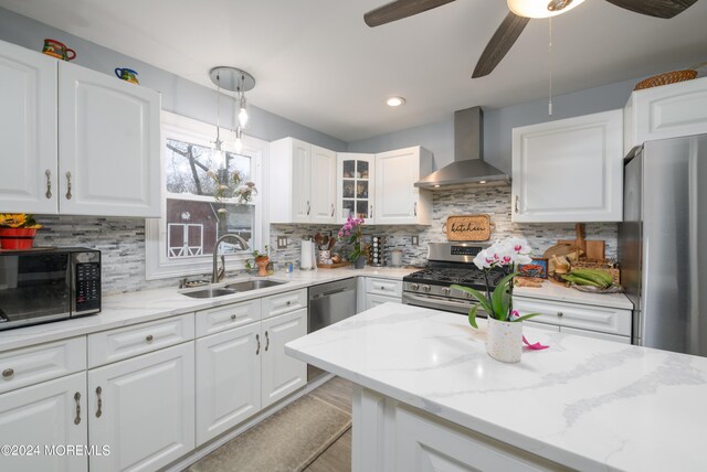 kitchen featuring light stone counters, a sink, white cabinetry, appliances with stainless steel finishes, and wall chimney exhaust hood